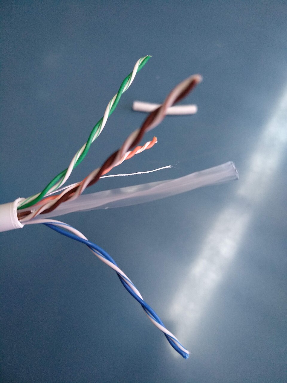 A Cat 5e cable with the outer sheath cut back, the four pairs fanned out and still twisted: green, brown, orange and blue, each wound against a white partner.